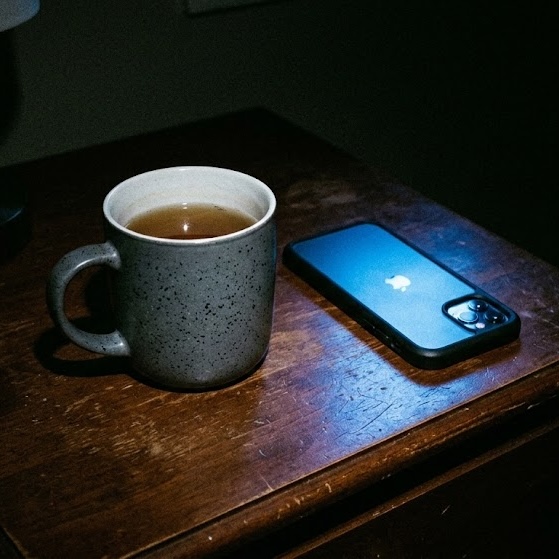 A mug of tea beside a phone on a dark wooden table at night